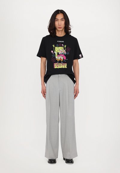 Black graphic t-shirt featuring colorful SpongeBob design, paired with light gray wide-leg trousers. The outfit is complemented by black shoes.