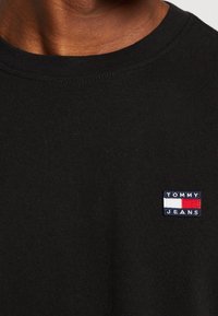 Černé bavlněné tričko s malým vyšitým logem Tommy Jeans v modré, červené a bílé na levé části hrudníku. Klasický design s kulatým výstřihem.