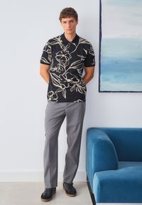 Juoda trumpomis rankovėmis palaidinė su smėlio spalvos gėlių raštu, pilkos pritaikytos kelnės ir juodi sportbačiai su guminėmis padomis. Švelni medžiaga ir laisvas kirpimas.