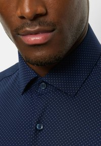 Navy blue shirt featuring a dotted pattern, constructed from a smooth fabric with a structured collar and matching button accents.