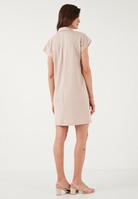 Robe rose clair à manches courtes avec col, coupe droite et couture dans le dos. Tissu lisse ; le modèle porte des sandales à talons beiges.