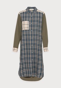 Robe chemise à boutons, présentant un motif écossais bleu marine et beige, des manches vert olive, une poche à rabat et un ourlet arrondi.