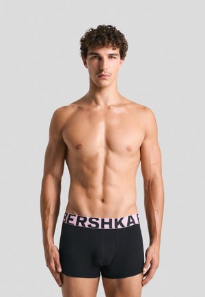 Schwarze Boxershorts aus weichem Stoff mit einem breiten rosa Bund, der "BERSHKA" in fetter Schrift zeigt. Die Passform ist eng und konturiert.