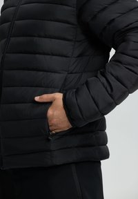 Sort puffjakke med quiltet design og lynlåslommer. Ærmerne er elastiske, hvilket forbedrer pasform og varme. Blød, glat tekstur.