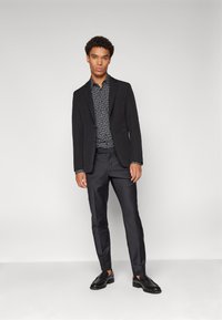 Blazer negru peste o cămașă închisă, modelată, asociată cu pantaloni închiși și mocasini negri. Design slim-fit, material neted și accente croite.