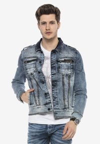 Leren spijkerjack in lichtblauw met studs, met twee borstzakken, een knopenfront en een contrasterende donkere kraag. Draag het over een wit shirt.
