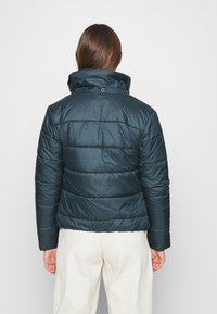 Mörk teal puffjacka med hög krage, quiltat mönster och knäppt stängning vid halsen. Har en slät, glänsande yta.