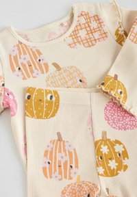 Ribbed cotton-vaate, jossa on erilaisia värikkäitä kurpitsakuoseja keltaisena, vaaleanpunaisena ja oranssina vaaleanbeigeällä taustalla. Nepeli kauluksessa.
