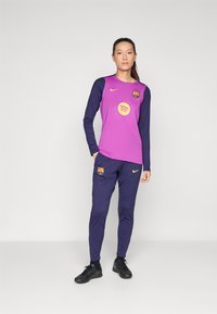 Haut de sport à manches longues violet avec des manches bleu foncé, logo Spotify et écusson du FC Barcelone ; associé à un pantalon bleu foncé assorti.