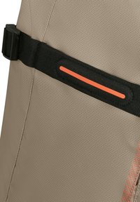 Beige texturerat tyg med ett justerbart svart band med en orange accent. Designen fokuserar på hållbarhet och användbarhet.