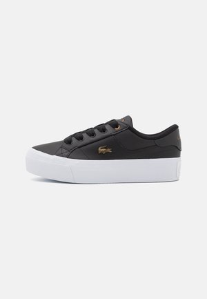 Sort lavtop sneaker med hvid tyk sål, sorte snørebånd og lille guld krokodille logo på siden.