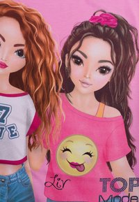 Zwei Charaktere im Cartoon-Stil auf einem rosa Hintergrund. Der eine trägt ein weißes und pinkes Cropped-Top; der andere trägt ein pinkes Shirt mit einem lächelnden Emoji-Graphic.