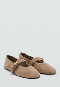 Beige nubuk ballet flats dengan ujung bulat, sabuk tunggal di bagian atas, dan detail gesper perkakasan emas. Tekstur halus dan sol datar.