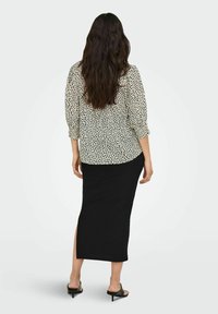 Blouse met een crèmekleurige achtergrond en zwarte abstracte vlekken, gecombineerd met een strakke zwarte geribbelde maxi rok met een zijsplit.