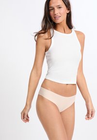 Biały bawełniany crop top w połączeniu z beżową, bezszwową bielizną. Top ma wysoki dekolt i dopasowany krój, podczas gdy bielizna charakteryzuje się gładkim, minimalistycznym stylem.