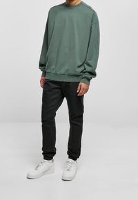 Sweatshirt vert surdimensionné avec un col rond, manches longues, poignets côtelés, associé à un pantalon de jogging noir slim et des baskets blanches.
