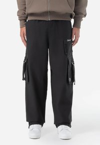 Black cargo pants made of durable fabric, featuring side pockets, a casual fit, and a logo patch on the front right pocket. Standard length.