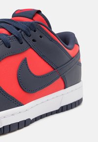Gros plan d'une basket basse bleu marine et rouge avec des lacets bleu marine et une semelle blanche.
