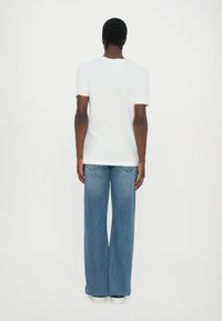 Hvit kortermet T-skjorte kombinert med vide blå denimjeans. Jeansene har en middels vask og en avslappet passform. Hvite sneakers fullfører antrekket.
