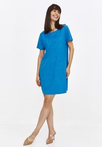 Jasnoniebieska sukienka z krótkim rękawem o luźnym kroju. Wykonana z gładkiego, teksturowanego materiału. Długość do kolan, zestawiona z cielistymi, szpiczastymi butami.