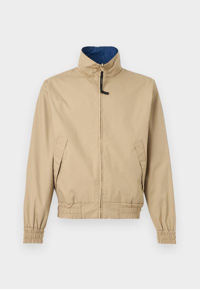 Μπεζ ελαφρύ μπουφάν με όρθιο γιακά, φερμουάρ μπροστά, δύο πλαϊνές τσέπες, ελαστικά μανίκια και μέση, επενδυμένο με γαλάζιο ύφασμα στο εσωτερικό του γιακά.