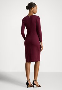 Pielāgojama ceļgalu garuma kleita burgundijas krāsā ar garām piedurknēm, aizmugurējo rāvējslēdzēju un gludu virsmu, kopā ar melnām augstpapēžu sandaletēm.