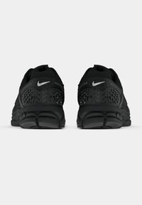 Τα μαύρα αθλητικά παπούτσια Nike διαθέτουν ένα υφασμάτινο άνω μέρος με γεωμετρικό σχέδιο, μαλακή σόλα και ένα μικρό λευκό λογότυπο στη φτέρνα.