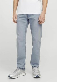 Jean léger bleu clair avec coupe slim, design à cinq poches et dégradé subtil. Assorti à des chaussures de sport argentées et un t-shirt blanc.