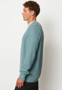 Hellblaues, geripptes Sweatshirt mit langen Ärmeln, rundem Ausschnitt und einem kleinen Etikett an der unteren linken Seite. Glatte Textur, lässiges Design.