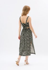 Schwarzes midi Kleid mit floralem Muster, tailliertem Oberteil, verstellbaren Spaghetti-Trägern und einer Schleife auf dem Rücken. Mit seitlichen Schlitzen und einem leichten Stoff.