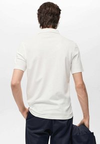 Witte polo met korte mouwen gezien vanuit de rug, met een klassieke kraag en een gladde textuur, gecombineerd met donkerblauwe broek.