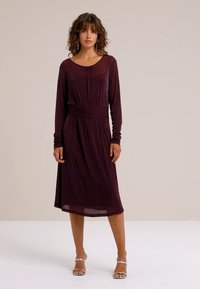 Burgunderfarbenes Langarmkleid mit tailliertem Schnitt und fließendem Rock. Glatte Textur, knielang, runder Ausschnitt, dezenter Glanz.