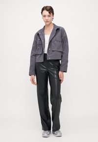 Cropped gray jacket with two front pockets, closed with zippers, worn over a white top and black faux leather pants. Silver sneakers complete the look.