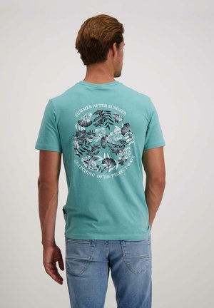 Turquoise katoenen t-shirt met een cirkelvormige bloemenafbeelding op de rug en de tekst "ZOMER NA ZOMER" en "OP ZOEK NAAR DE PERfectE GOLF."