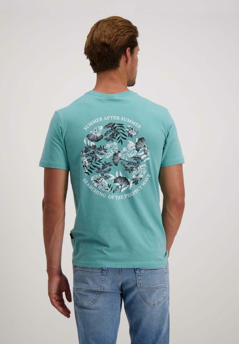 Turquoise katoenen t-shirt met een cirkelvormige bloemenafbeelding op de rug en de tekst "ZOMER NA ZOMER" en "OP ZOEK NAAR DE PERfectE GOLF."