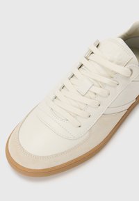 Białe skórzane i jasnoszare zamszowe sneakersy z beżową gumową podeszwą, z płaskimi sznurowadłami, wyściełanym językiem i subtelnymi detalami stębnowania.
