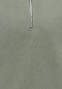 Gros plan sur un tissu vert clair avec une fermeture éclair verticale argentée partiellement ouverte.