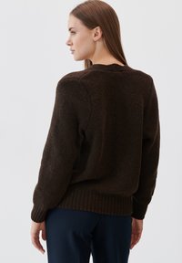 Brązowy sweter dziany z teksturowanej tkaniny, z prążkowanymi mankietami i dołem. Widoczny z tyłu, charakteryzujący się luźnym krojem i okrągłym dekoltem.