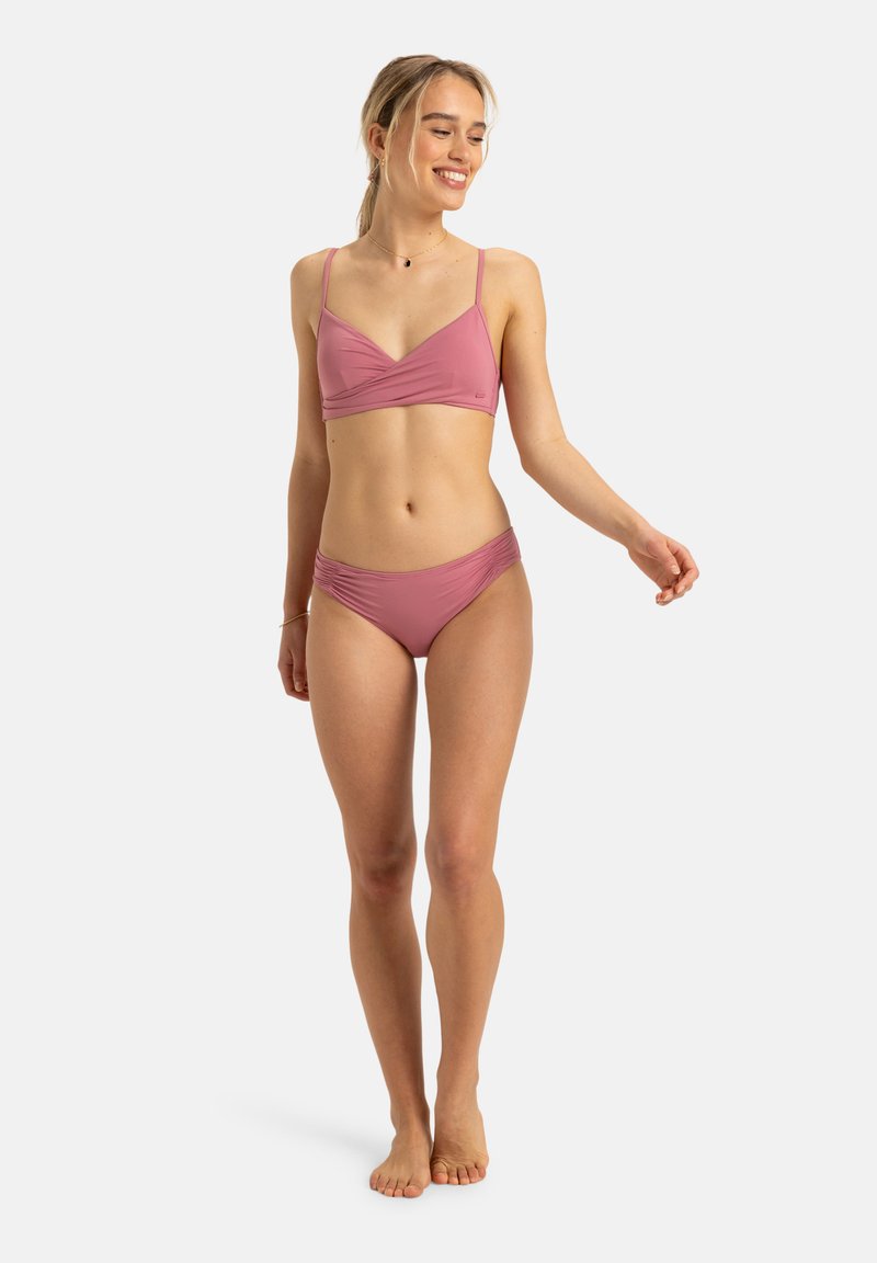 Bikini-Set in gedecktem Rosa, bestehend aus einem umwickelten Bralette mit schmalen Trägern und passenden gerafften Bikini-Unterteilen, gefertigt aus glattem, dehnbarem Material.