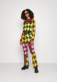 Conjunto de duas peças com padrão argyle colorido em preto, rosa, verde, amarelo e vermelho, com um design justo; combinado com botas largas pretas.