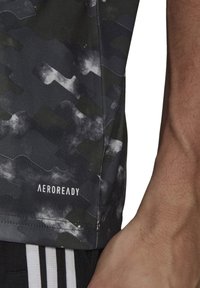 Maglietta sportiva con motivo mimetico nero e grigio, con il marchio "AEROREADY" lungo l'orlo. Tessuto morbido e design moderno per abbigliamento da prestazione.