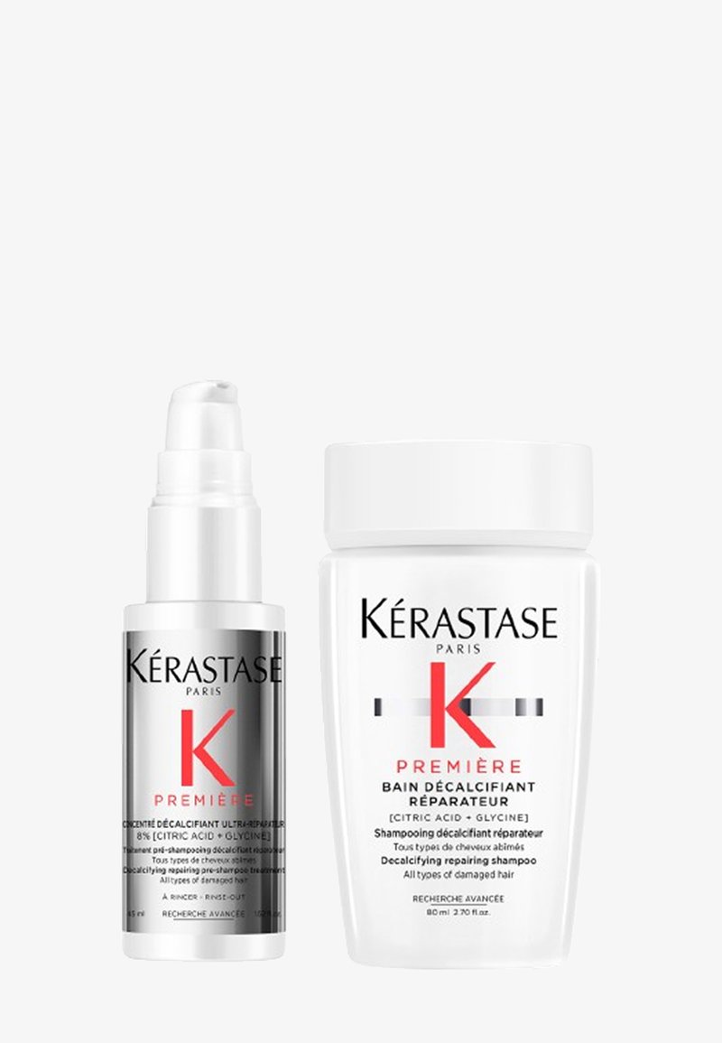 Set di prodotti per la cura dei capelli Kérastase con una bottiglia a pompa argento e un barattolo bianco, entrambi etichettati con accenti rossi e testo chiaro che dettaglia il tipo di prodotto.