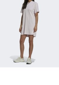 Różowa sukienka z krótkim rękawem, wykonana z bawełny o luźnym kroju, z zaokrąglonym dołem. Połączona z jasnymi sportowymi butami.
