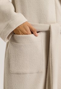 Robe beige con texture, maniche ampie, vita legata e tasche laterali. Il tessuto appare morbido e lanuginoso, adatto per il comfort.