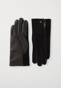 Gants en cuir noir avec des accents en suede, présentant une texture lisse, des doigts droits et un détail de logo. Design classique avec un poignet ajusté.