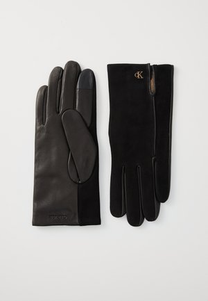 Gants en cuir noir avec des accents en suede, présentant une texture lisse, des doigts droits et un détail de logo. Design classique avec un poignet ajusté.