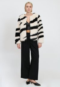 Faux fur jakke med sort-hvide striber, oversized design og blød tekstur. Sættet er kombineret med sorte brede bukser og spidse sko.