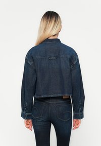 Cropped spijkerjasje in donkerblauw, met lange mouwen, knopenmanchetten en een rechte zoom. Effen achterkant met subtiele stikdetails.