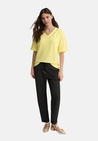 Top giallo a V, con maniche corte, abbinato a pantaloni neri con cordoncino. Accenti dorati notevoli nelle calzature. Design semplice e moderno.