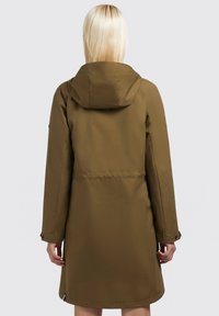 Oliivinvihreä, puolipitkä takki hupulla, säädettävillä hihoilla ja nyöritetyllä vyötäröllä. Tasainen, vettä hylkivä kangas minimalistisella muotoilulla.
